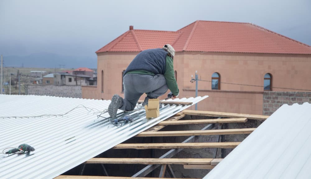 man installing sheets metal tiles to repair roof