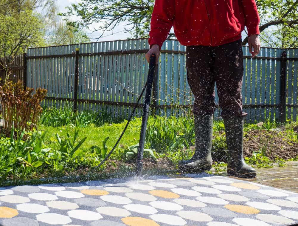 man washing carpet with pressure washer outdoors